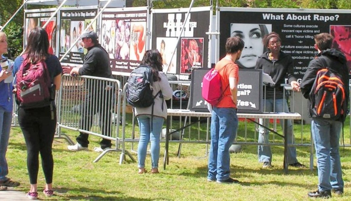 Center for Bio-Ethical Reform (CBR) Staff interact with Students at University North Carolina (UNC) Greensboro. Behind them are numerous vinyl banners comparing abortion to other forms of genocide.