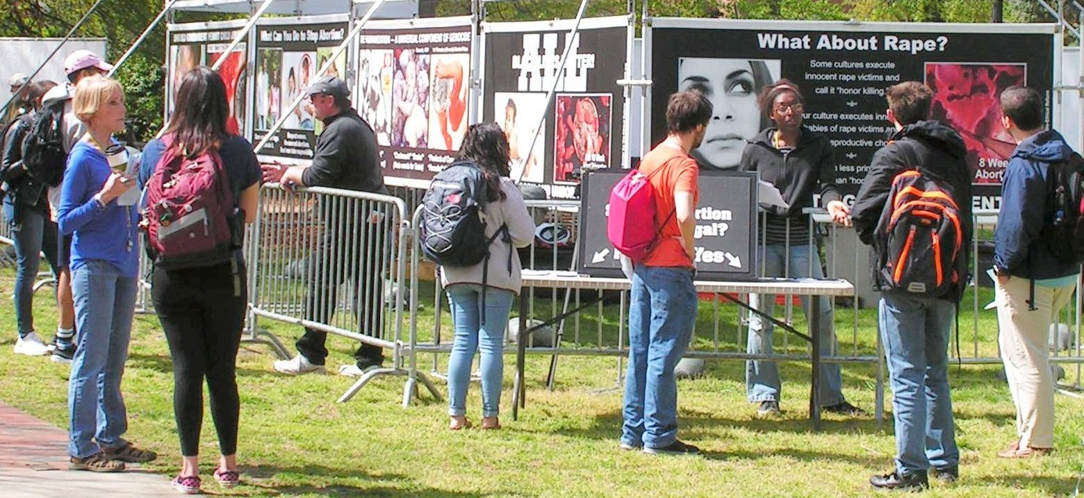 Center for Bio-Ethical Reform (CBR) Staff interact with Students at University North Carolina (UNC) Greensboro. Behind them are numerous vinyl banners comparing abortion to other forms of genocide.
